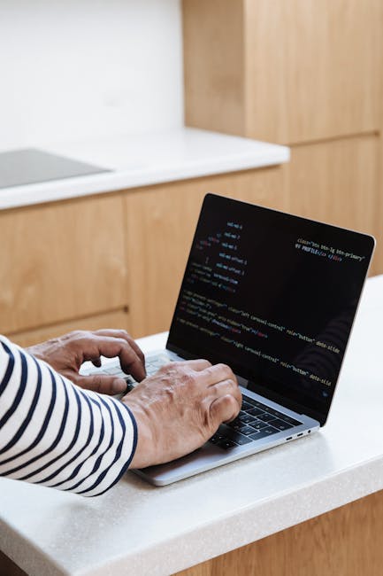 A person sitting in a vehicle using a laptop to perform garden maintenance planning, with the laptop screen displaying lines of code and a web-based interface. The individual is slightly out of focus,